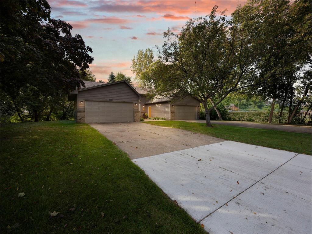 Front exterior of a side-by-side twin home at 5535–5537 Lindsay St in Golden Valley, MN with two garages, tree-lined yard at twilight.